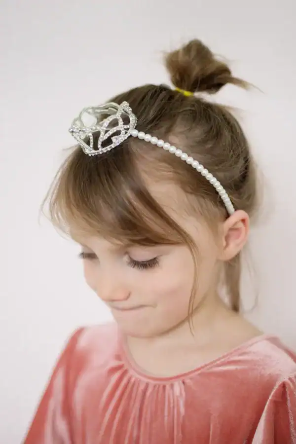 Child wearing crown headband and pink velvet dress.