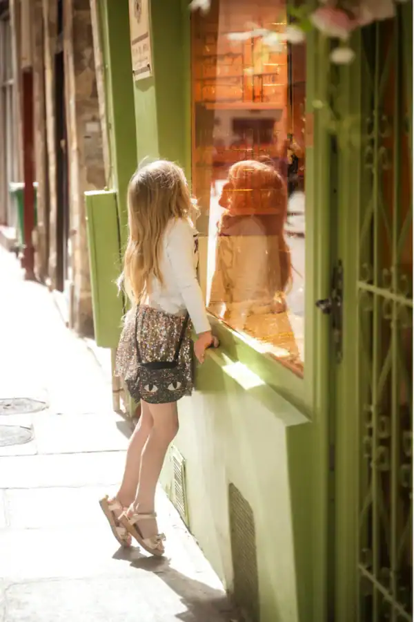 Girl looking into shop window, green exterior.