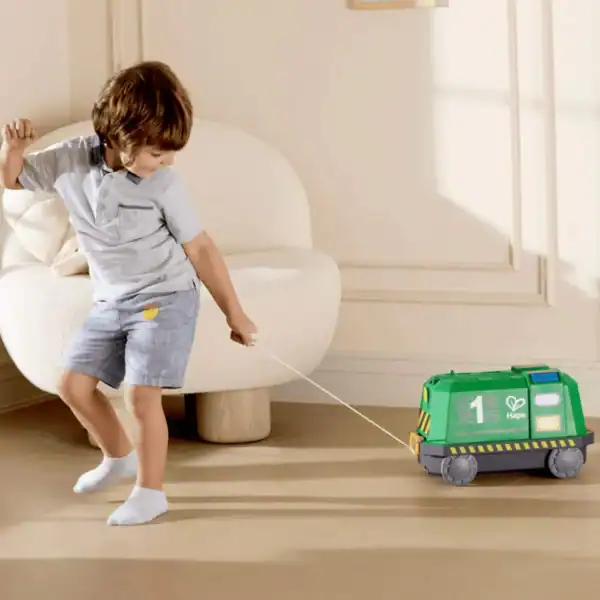 Child pulling green toy vehicle indoors.