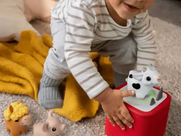 Toddler playing with toy cow on red speaker.