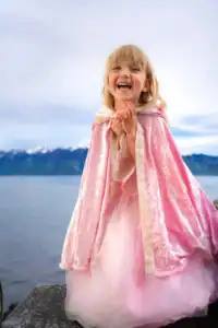 Smiling child in pink dress by a lake.