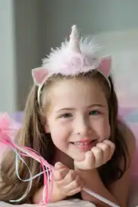 Girl in unicorn headband smiling with wand.