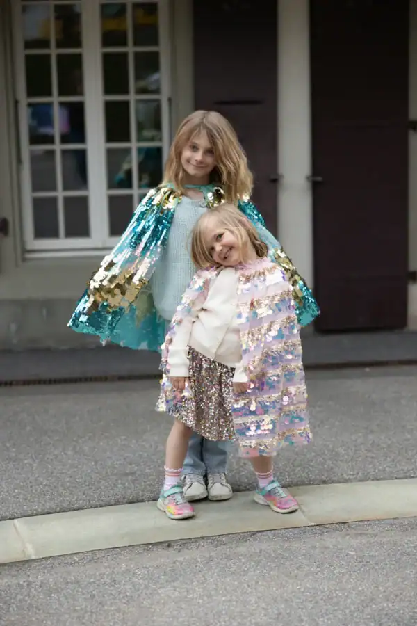 Two children wearing colorful sequin capes