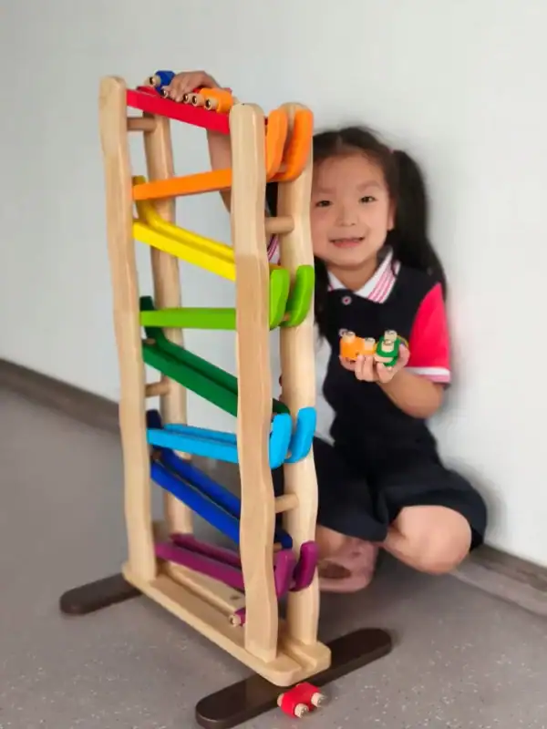 Child playing with wooden rainbow ball track.