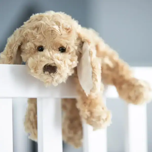 Plush dog toy resting on a crib rail