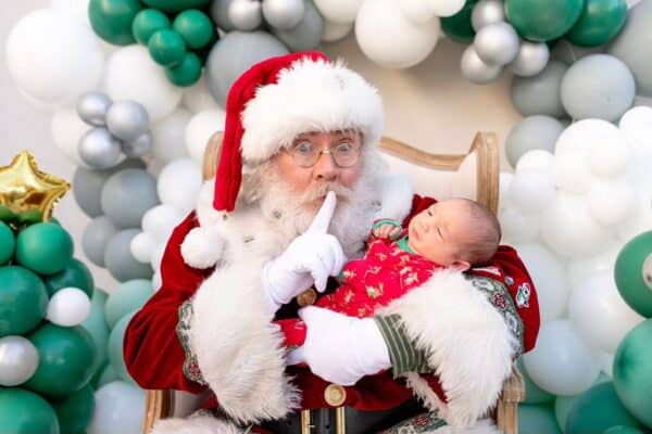 Santa holding baby with festive balloon backdrop