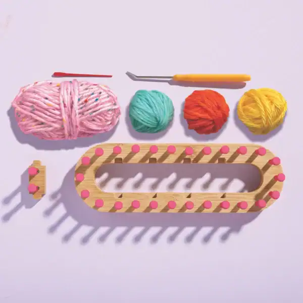 Wooden knitting loom with colorful yarn and tools.