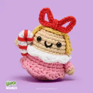 Crochet doll holding candy cane on purple background.