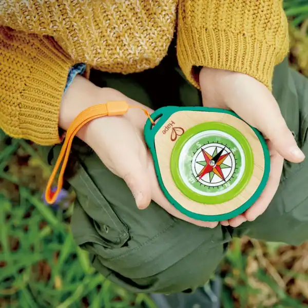 Child holding colorful compass outdoors.