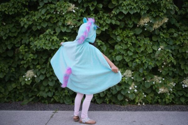 Child in unicorn costume near green foliage.