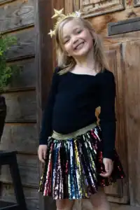 Smiling child in sparkly skirt and star headband.