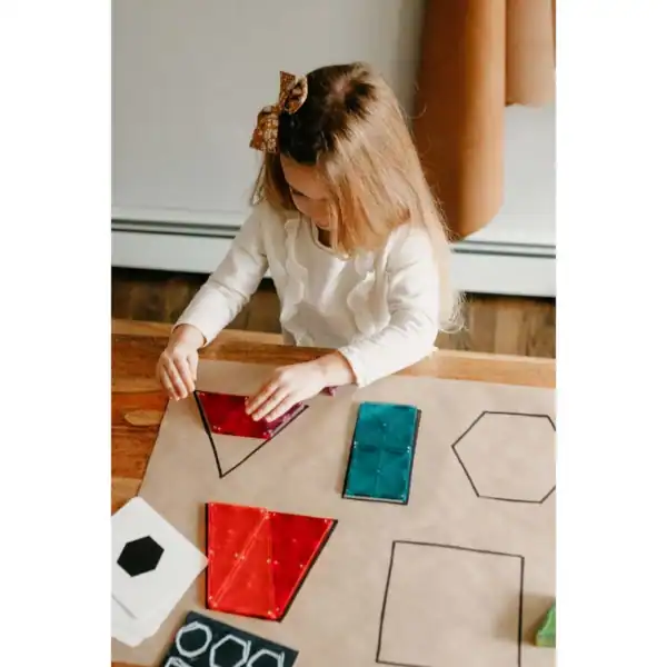 Child assembling colorful geometric shapes on paper.