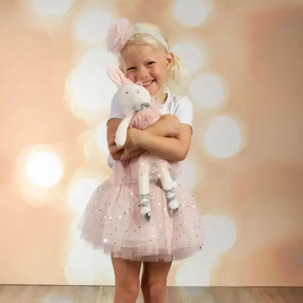 Smiling child hugging plush bunny in pink dress.