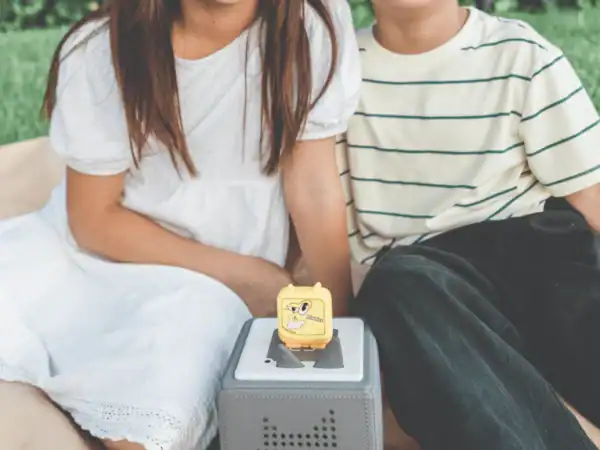 Children playing with a cube-shaped speaker outdoors.